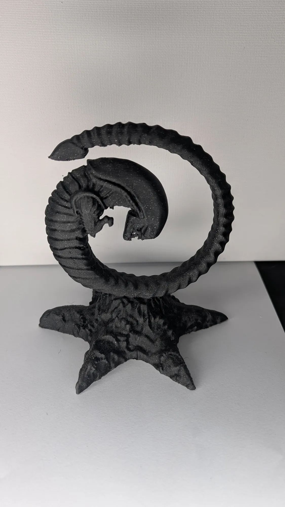Statue décorative du chestburster d'Alien imprimée en 3D en filament noir, enroulée sur un socle étoilé